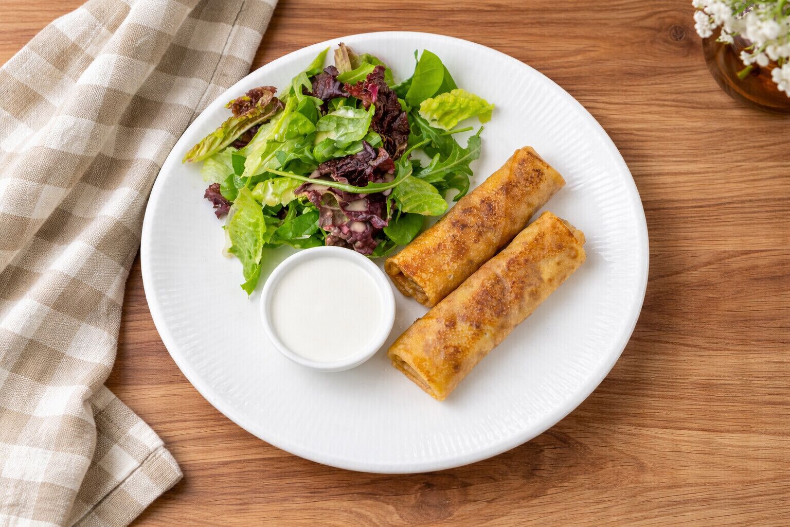 A plate with spring rolls and a salad on a wooden table.