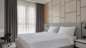 A modern hotel room with a large bed, a desk, and a chair. - STYLO Residences & Suites (Tashkent)