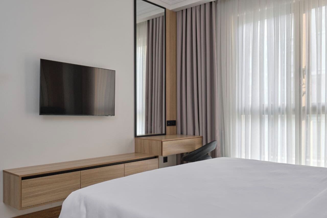 A modern hotel room with a large bed, a wooden desk, a flat-screen TV, and a large mirror.