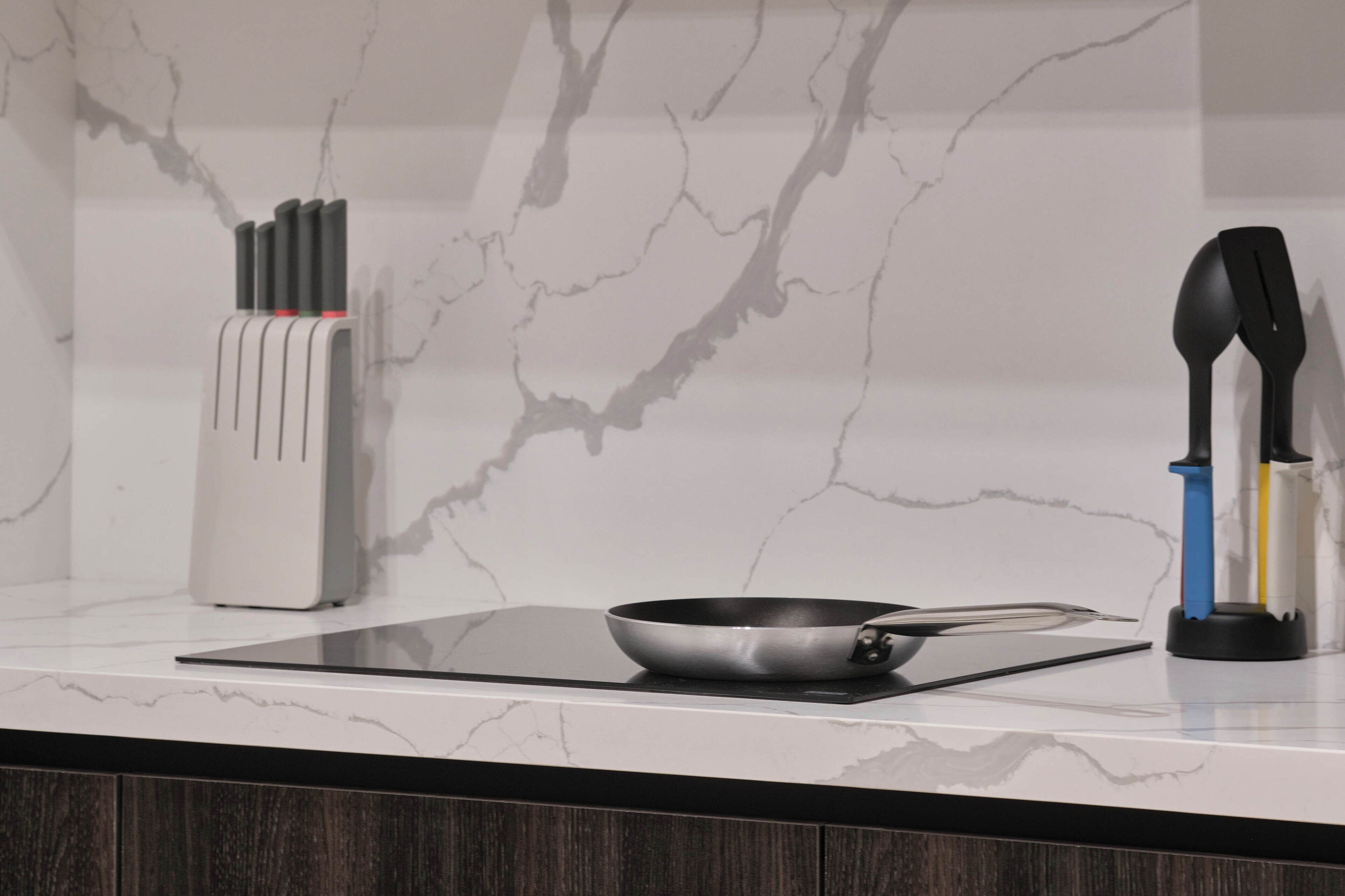 A kitchen counter with a frying pan, a knife block, and a spatula holder.