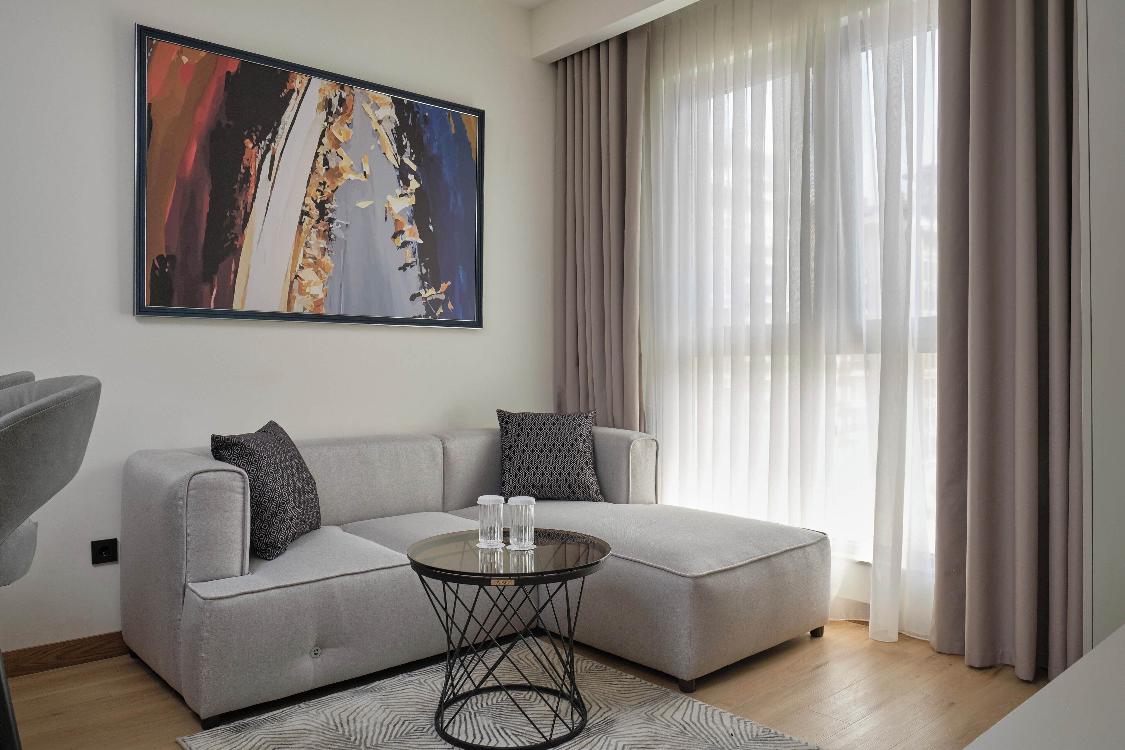 A modern living room with a grey sofa, two patterned pillows, a round coffee table, and a large abstract painting on the wall.