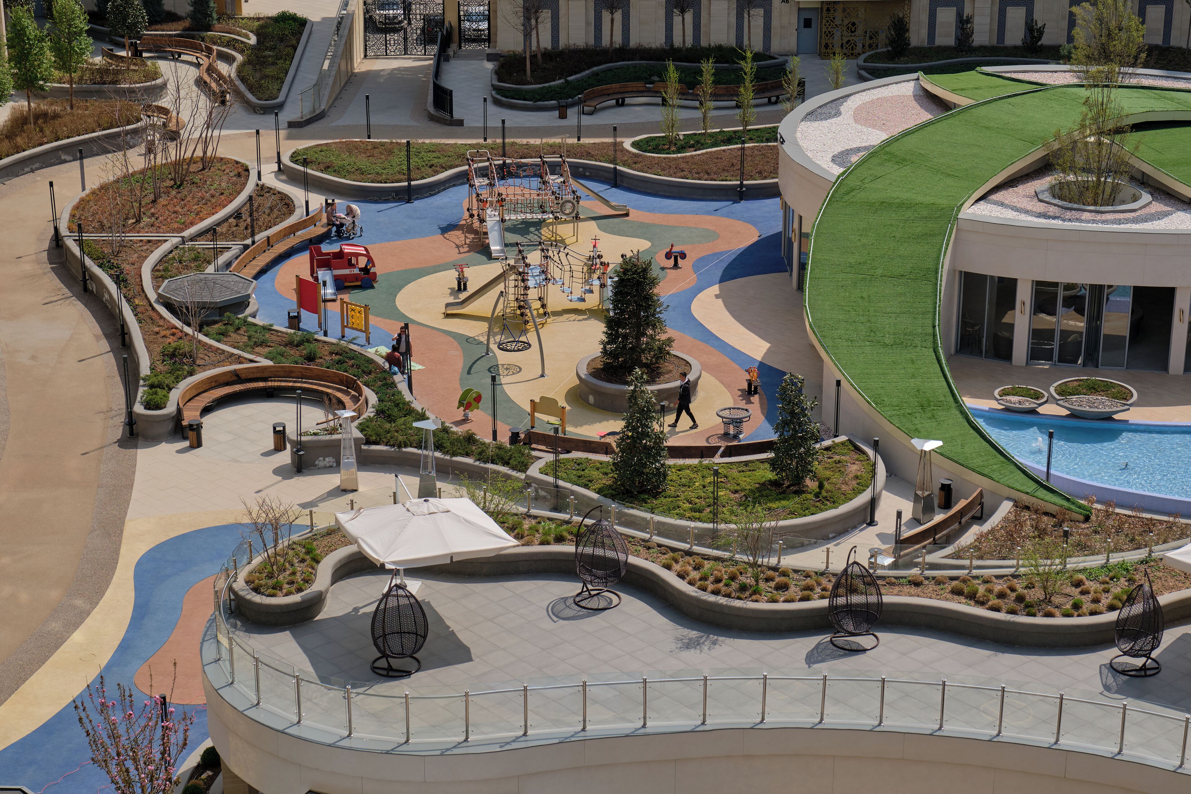 Un patio ajardinado con parque infantil, zonas de estar y piscina.