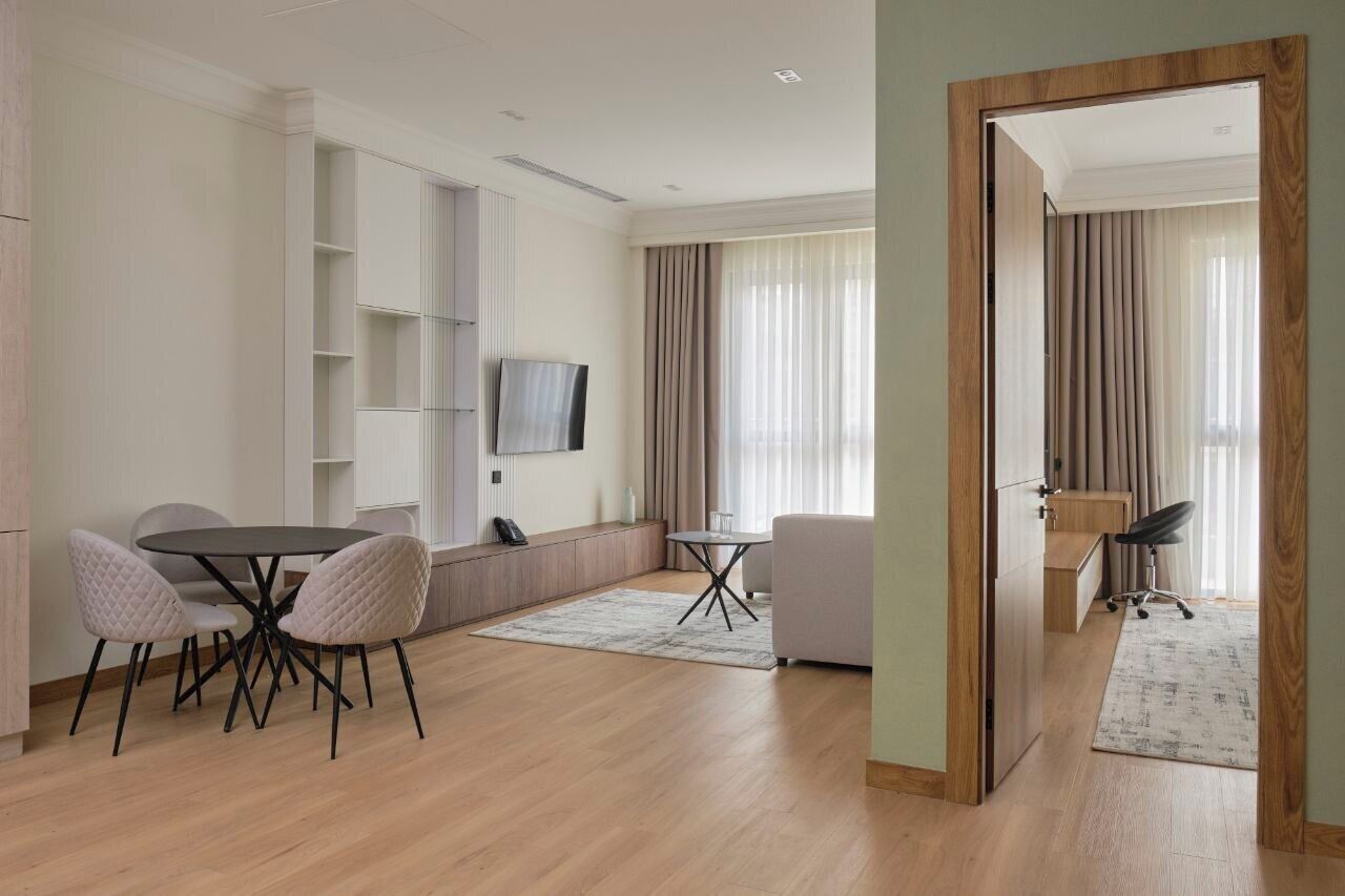 Ein modernes Wohnzimmer mit Essbereich, einem an der Wand befestigten Fernseher und einem großen Fenster mit Vorhängen.