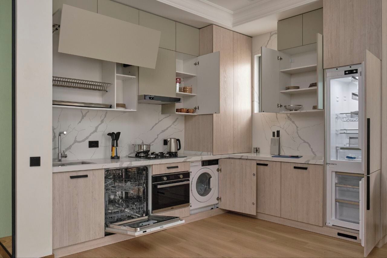 Une cuisine moderne dotée d’appareils électroménagers intégrés, notamment un lave-vaisselle, un four et un lave-linge, ainsi que de meubles de rangement en bois.
