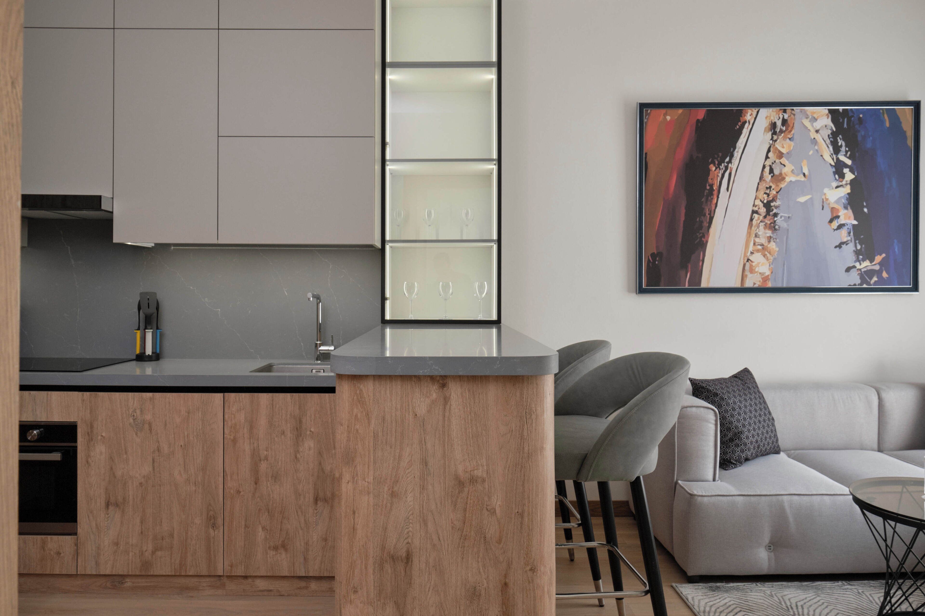 Une cuisine moderne avec des meubles en bois, un îlot central intégré et un coin repas comprenant un canapé et des chaises gris.