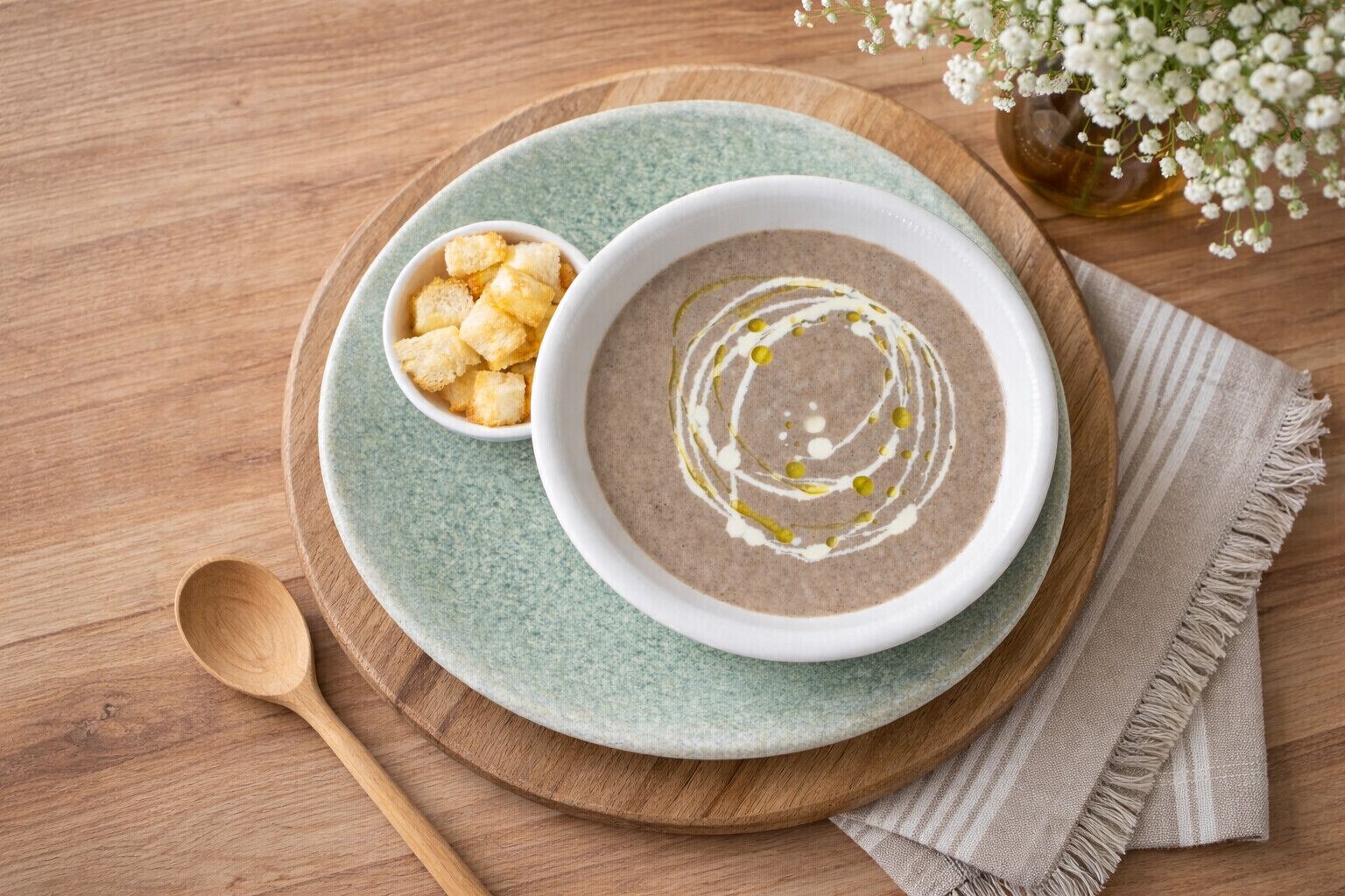En skål suppe med lidt olie og en lille skål brødcroutoner på et træbord.
