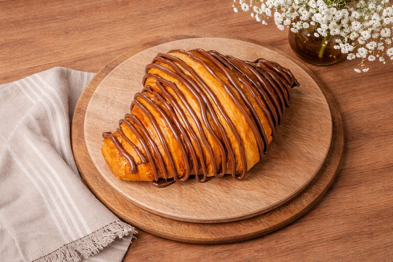 A croissant with chocolate drizzle on a wooden board.