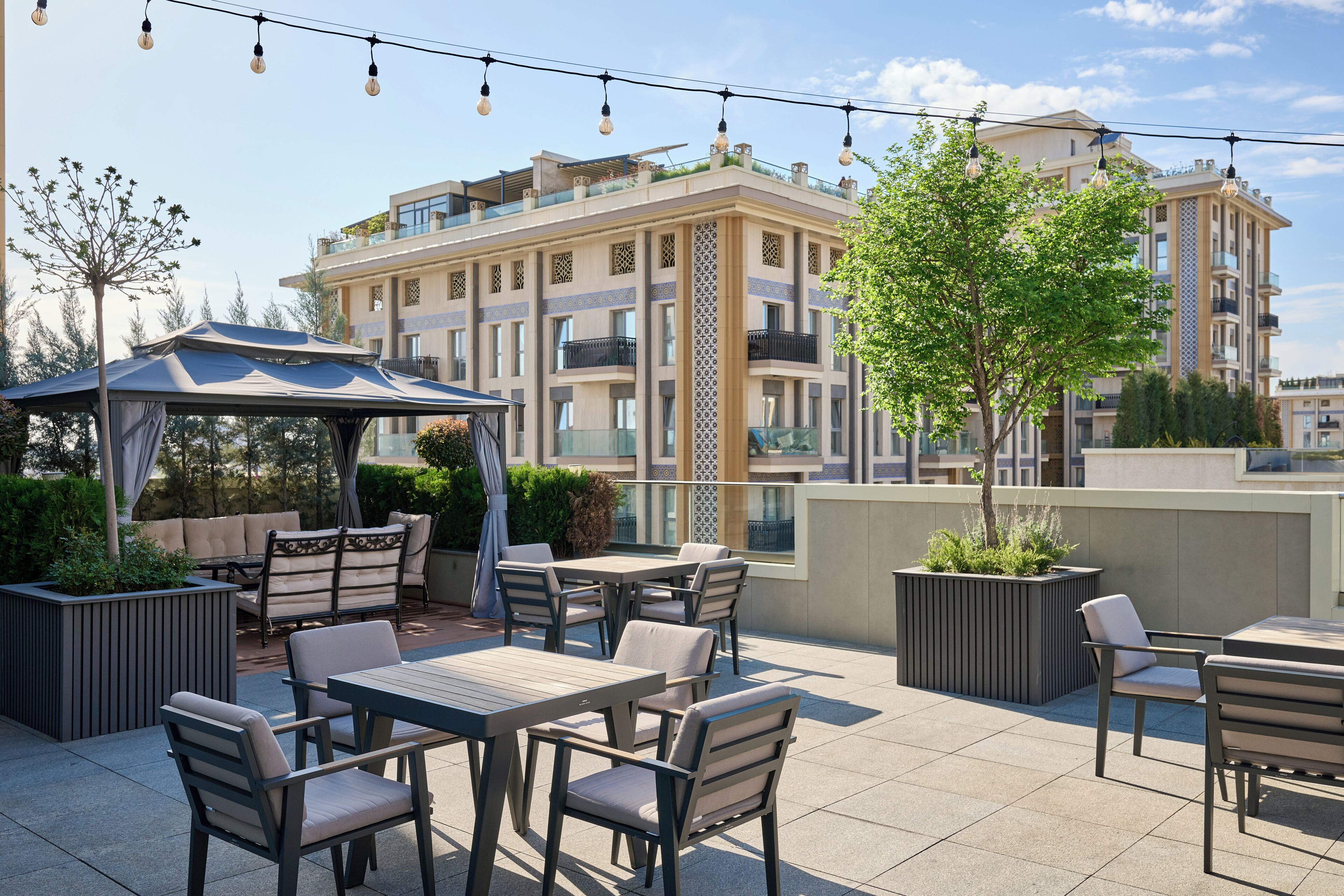 An outdoor patio with tables and chairs, a gazebo, and a view of a multi-story building.