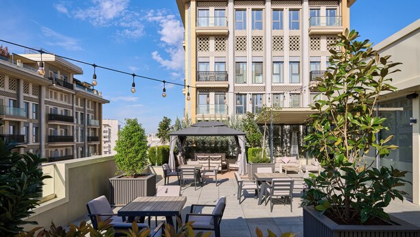 A rooftop patio with outdoor furniture, a pergola, and a view of a multi-story building. - STYLO Residences & Suites (Tashkent)