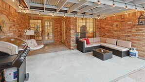 Un patio al aire libre con pared de ladrillo, una parrilla, un sillón colgante y un sofá con cojines.