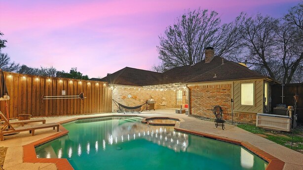 Un patio trasero con piscina, terraza de madera y una hamaca.