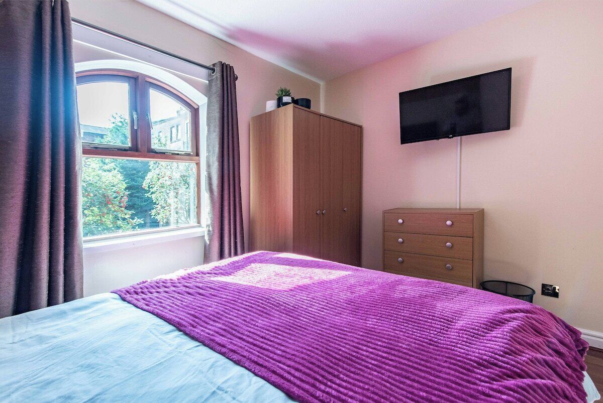 Ein Schlafzimmer mit Bett, Kleiderschrank, Kommode, Fernseher und einem Fenster mit Vorhängen.