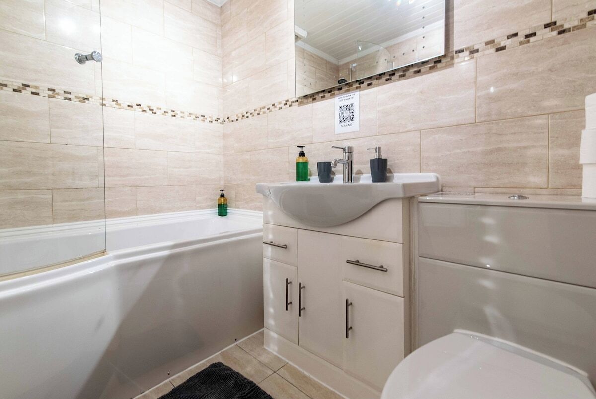 Une salle de bain avec une baignoire, un lavabo et des toilettes. Il y a un miroir au-dessus du lavabo et un code QR sur le mur.
