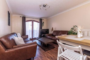 A living room with a brown leather sofa, a wooden coffee table, a TV, and a dining table with chairs. - 2BR Apartment in the Heart of Leeds City Centre (West Yorkshire)