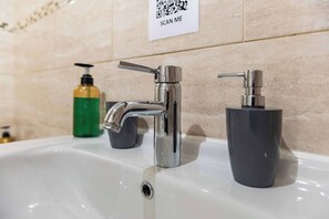 A bathroom sink with a chrome faucet, a soap dispenser, and a QR code sign on the wall. - 2BR Apartment in the Heart of Leeds City Centre (West Yorkshire)