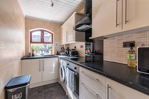 A compact kitchen with a washing machine, a sink, and a window with a view of greenery. - 2BR Apartment in the Heart of Leeds City Centre (West Yorkshire)