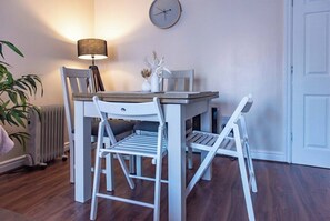 A dining area with a table and chairs, a lamp, a clock on the wall, and a radiator. - 2BR Apartment in the Heart of Leeds City Centre (West Yorkshire)