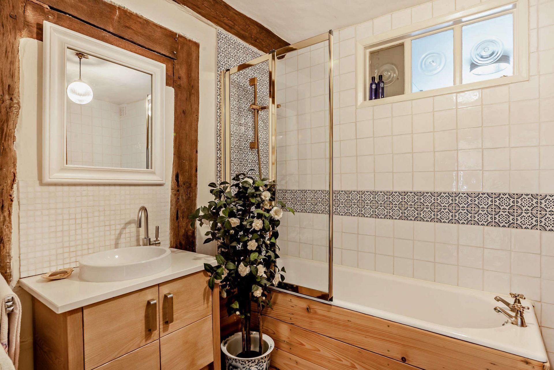 A bathroom with a wooden vanity, a large mirror, a sink, a shower with a glass door, and a decorative plant.