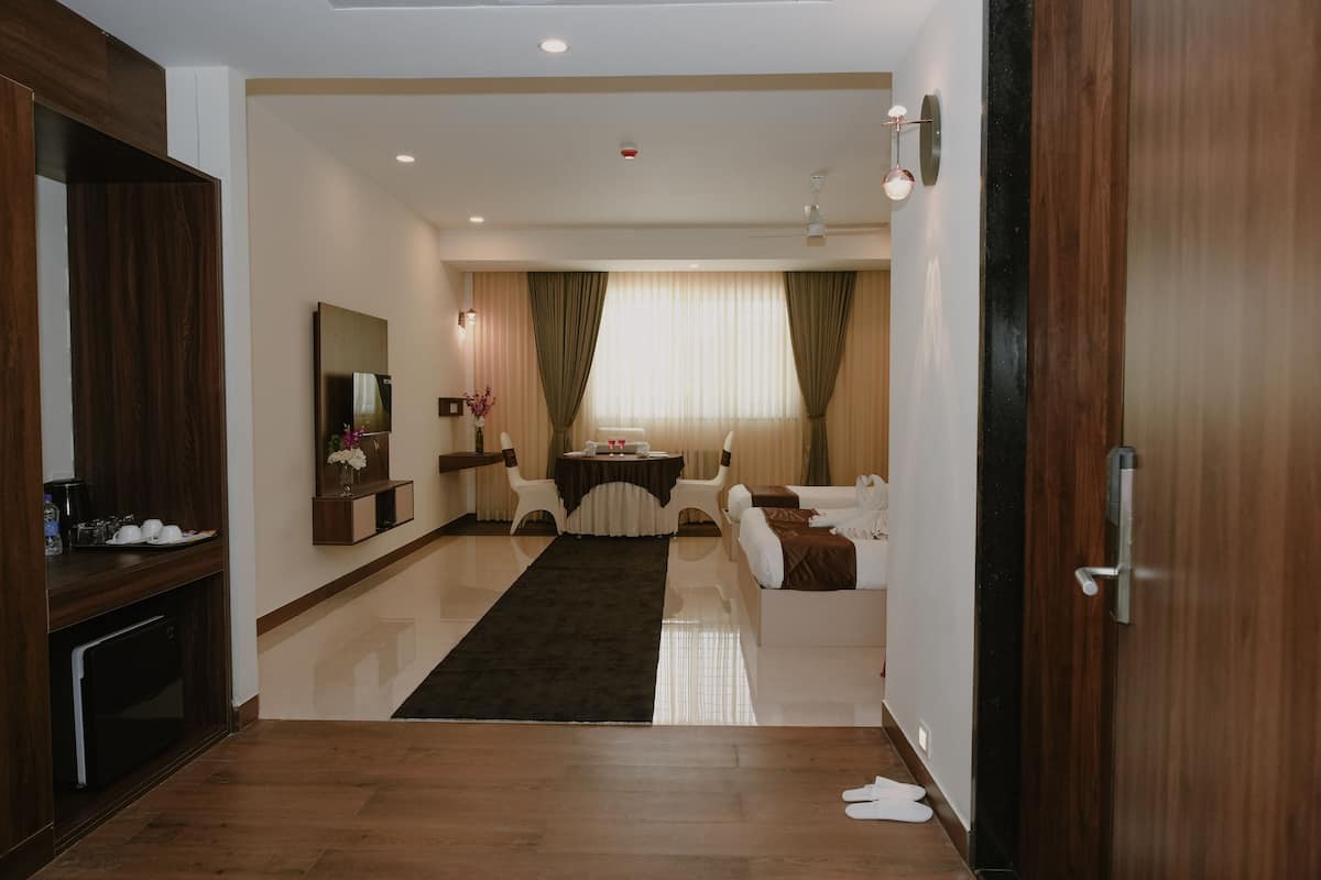Una habitación de hotel moderna con piso de madera, un rincón de comedor con mesa y sillas, un sofá y un espejo grande.