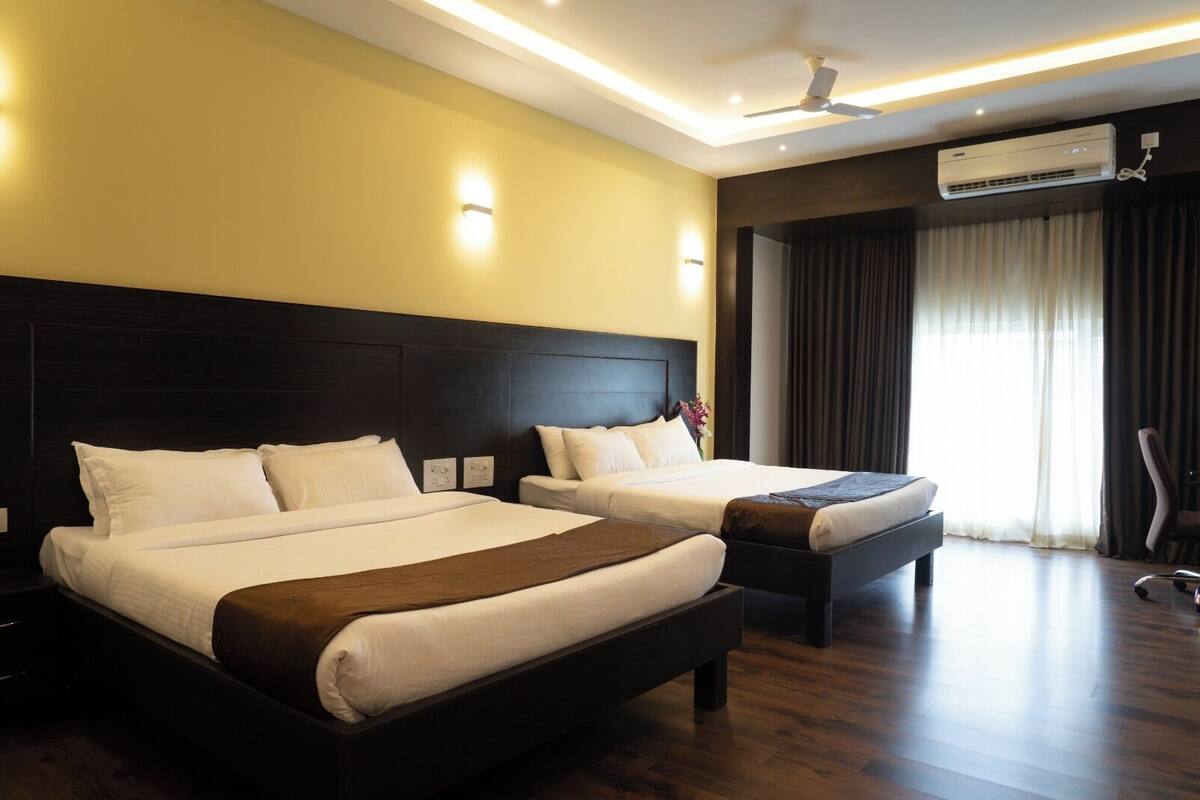 Habitación de hotel con dos camas, ventilador de techo, equipo de aire acondicionado y vista al exterior por la ventana.