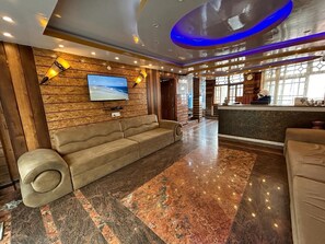 A lobby with a sofa, a TV, and a reception desk. - RATNA VILLA INN (Darjeeling)