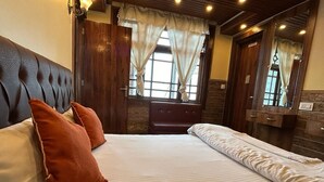 A hotel room with a large bed, a wooden headboard, a window with curtains, a mirror, and a wooden dresser. - RATNA VILLA INN (Darjeeling)