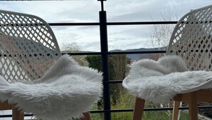 Twee witte stoelen met behaaglijke kussens op een balkon met een metalen hekwerk.