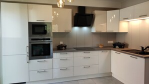 Een moderne keuken met witte kasten, roestvrijstalen apparatuur, een zwarte afzuigkap en hanglampen.