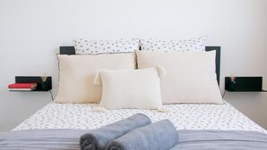 A neatly made bed with patterned bedding, a folded towel, and a bedside table with a book and a lamp.