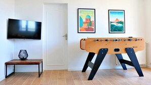 A room with a foosball table, a television mounted on the wall, and two framed pictures on the wall.