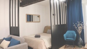 Een slaapkamer met een bed, een stoel, een spiegel en een vaas met takken.