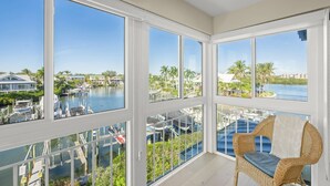 A balcony with a wicker chair, large windows, and a view of a marina and water. - Beautiful Condo, Waterfront, Dock Views, Walk to Private Beach, Heated Pools, Tennis, Pickleball (Siesta Key)