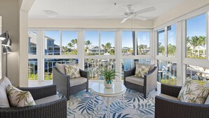 A spacious balcony with wicker furniture, a ceiling fan, and a view of the pool and surrounding buildings. - Beautiful Condo, Waterfront, Dock Views, Walk to Private Beach, Heated Pools, Tennis, Pickleball (Siesta Key)