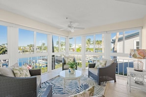 A sunlit room with large windows, a ceiling fan, wicker furniture, and a view of a marina. - On the Bay - great views! Walk to Priv Beach, Pool (Siesta Key)