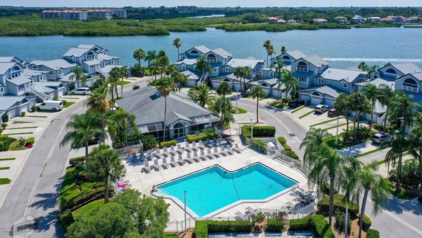 A resort with multiple blue-roofed buildings, a central swimming pool, and a view of a body of water. - Beautiful Condo, Waterfront, Dock Views, Walk to Private Beach, Heated Pools, Tennis, Pickleball (Siesta Key)