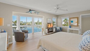 A bedroom with a bed, a desk, a chair, a TV, and a balcony with a view of the sea. - Beautiful Condo, Waterfront, Dock Views, Walk to Private Beach, Heated Pools, Tennis, Pickleball (Siesta Key)