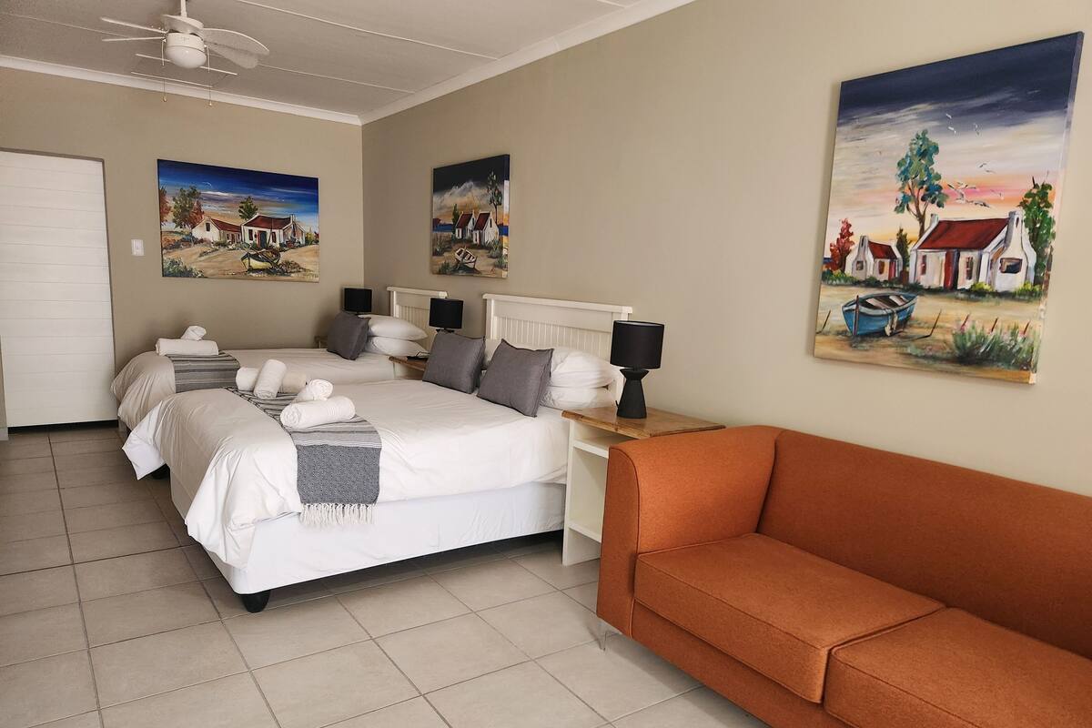 A hotel room with a bed, two bedside tables with lamps, a sofa, and two paintings on the walls.