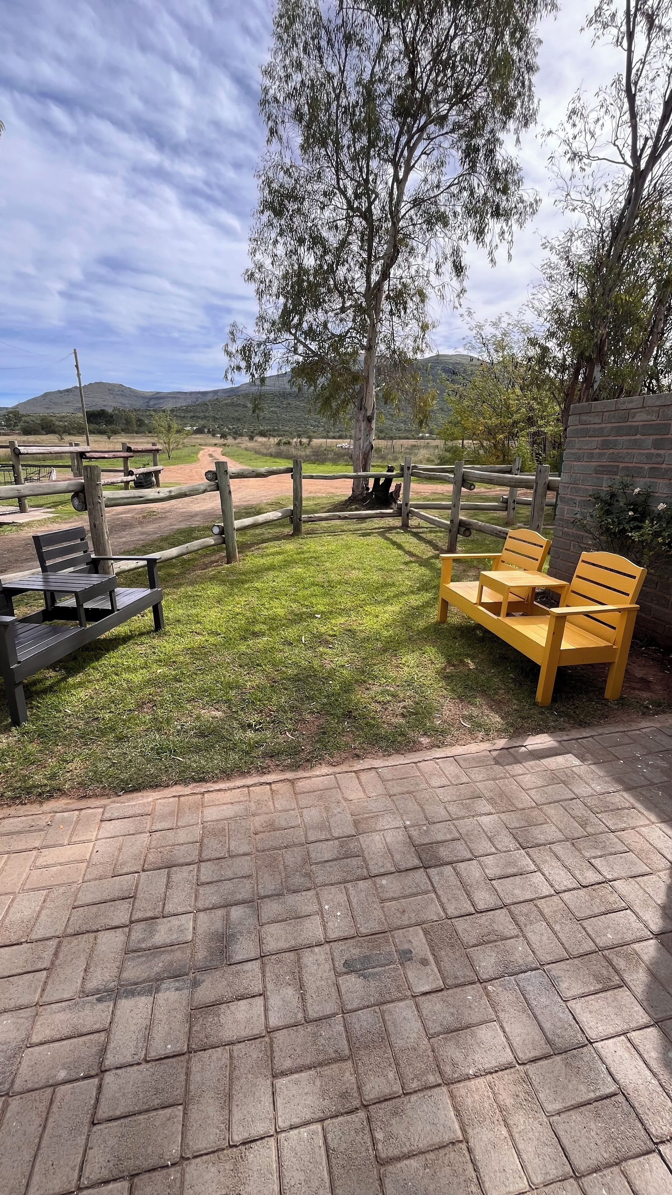 An outdoor seating area with a brick patio, wooden benches, and a table.