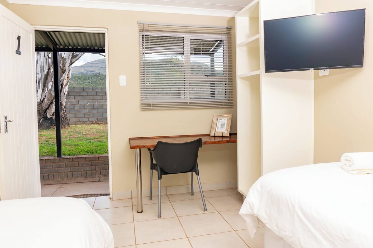 A hotel room with a bed, a desk with a chair, a television, and a window with blinds.