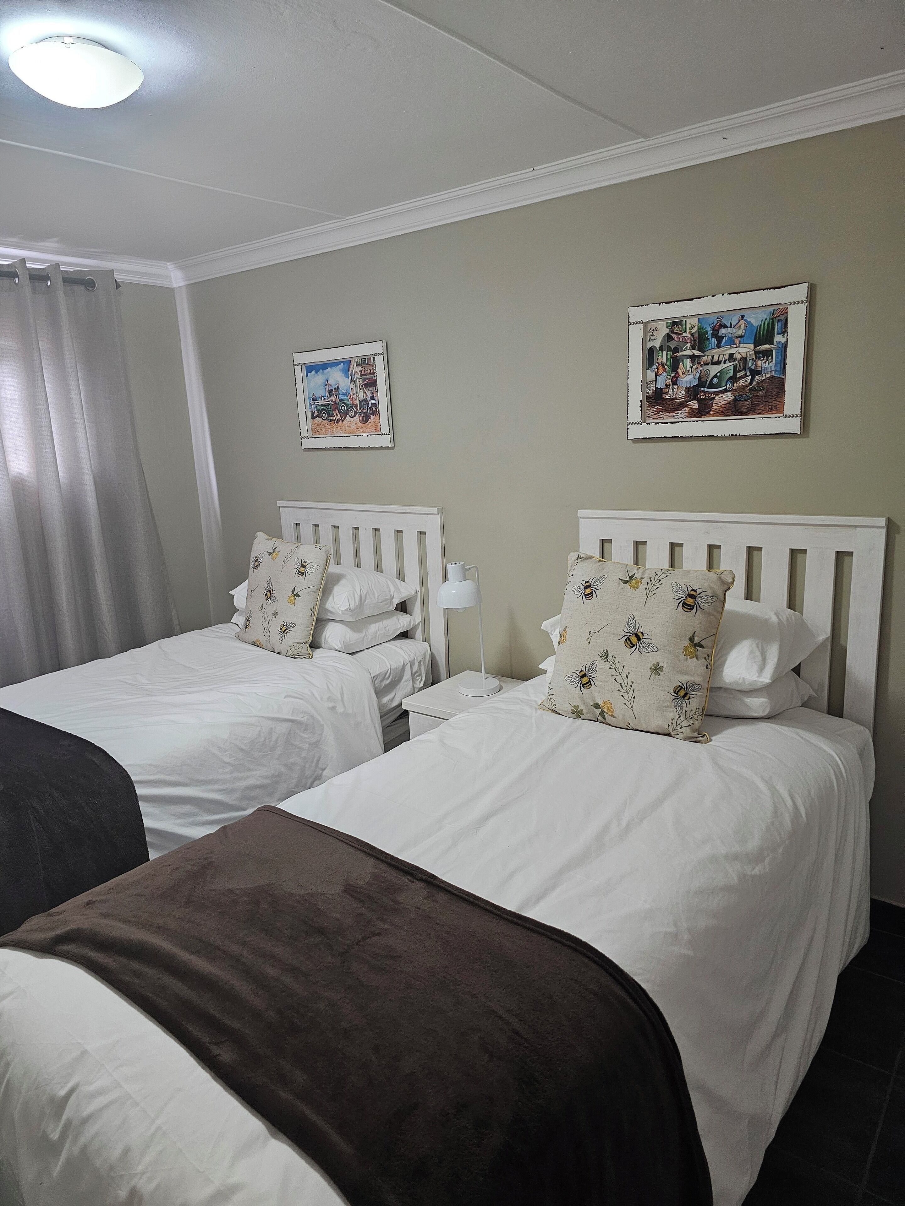A hotel room with two single beds, white bedding, and floral-patterned pillows.