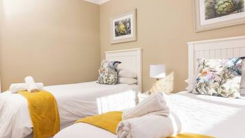 A hotel room with two beds, each with white linens and a yellow throw blanket. There is a white nightstand with a lamp and a framed picture on the wall.