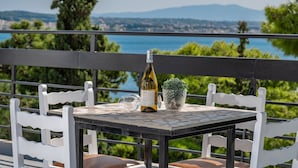 Une table avec une bouteille de vin, un verre et une plante en pot, sur un balcon donnant sur un paysage magnifique.