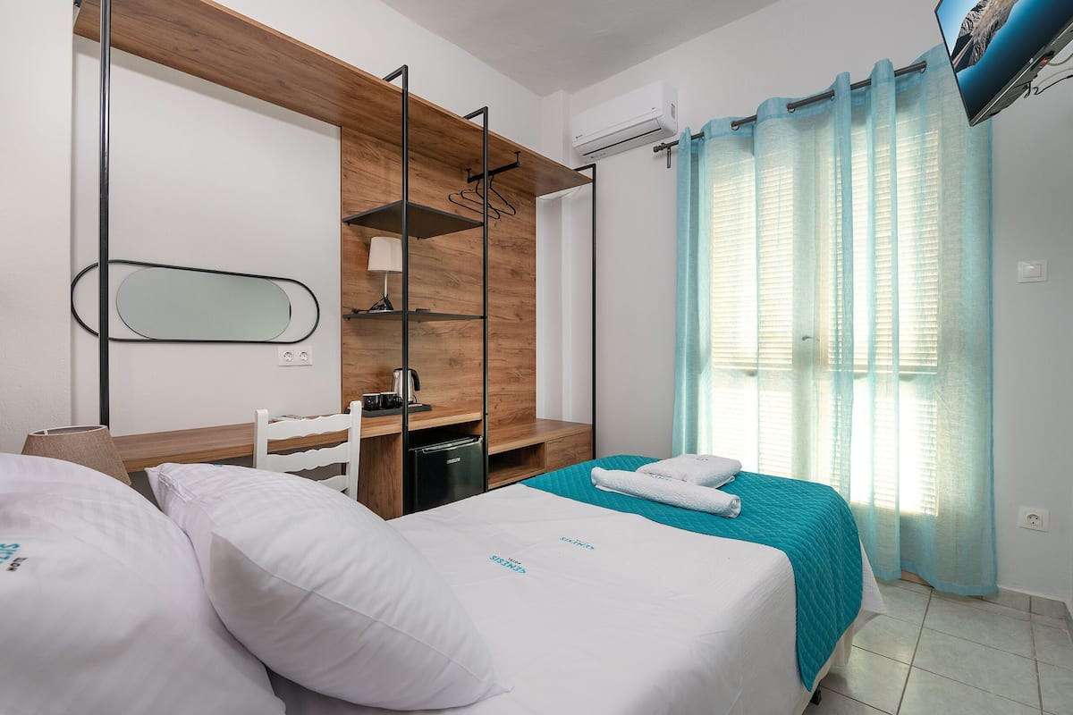 Habitación de hotel con dos camas, un armario de madera, un escritorio, un espejo y una ventana con cortinas.