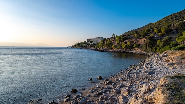 Un paysage côtier avec une rive rocheuse, un bâtiment à étages situé sur une colline et une mer calme.