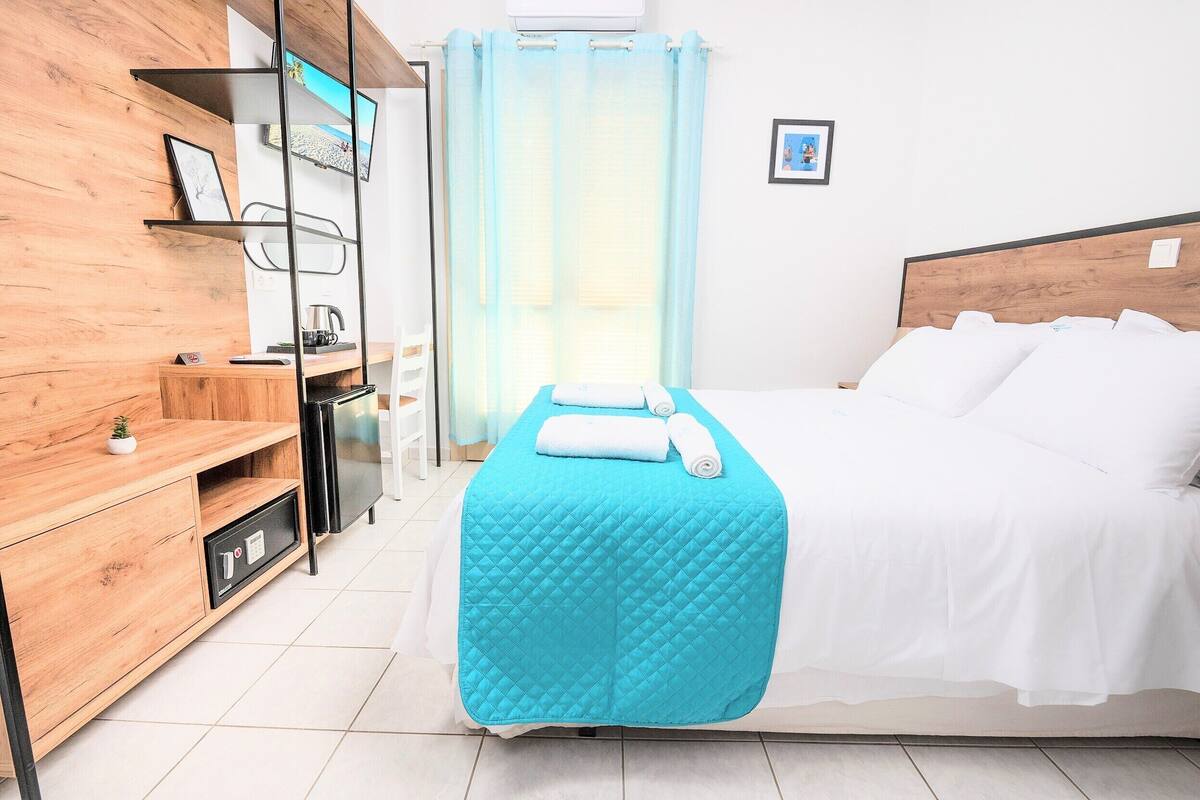 Habitación de hotel con una cama, una mesita de noche de madera, una repisa con un marco de foto y una ventana con cortina.