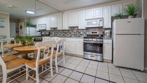 A modern kitchen with white cabinets, stainless steel appliances, and a wooden dining table with chairs. - 1911 Oceanblock Summa (Ocean City)