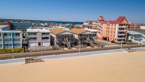 A beachfront hotel with multiple buildings, including a prominent red building with balconies and a white building with a wooden deck. - 1911 Oceanblock Summa (Ocean City)