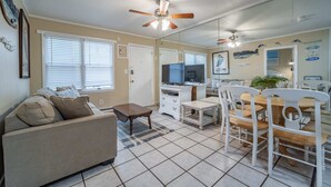 A living room with a sofa, coffee table, dining table, chairs, ceiling fan, TV, and a kitchen area with cabinets and a microwave. - 1911 Oceanblock Summa (Ocean City)