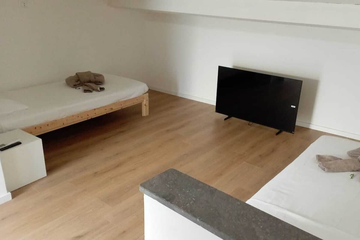 Une petite pièce, peu meublée, avec un plancher en bois, un lit, une télévision et une petite table.