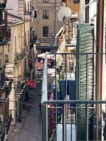 A narrow street with buildings on both sides, balconies with clothes hanging, and a small outdoor seating area.